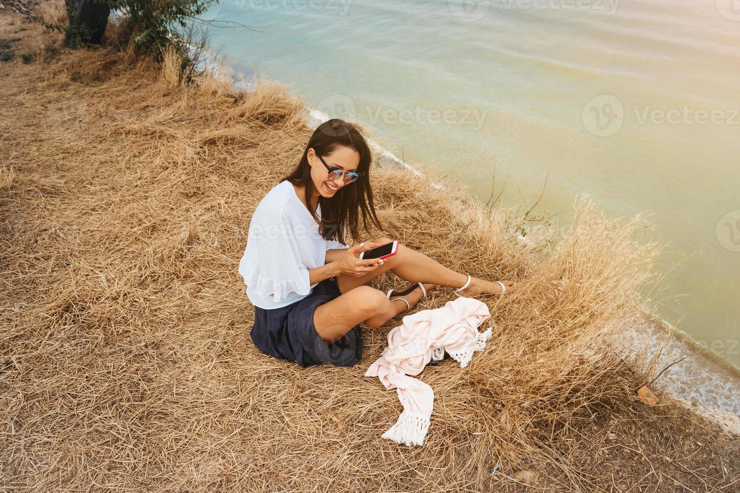 attractive woman in summer skirt and shirt sits on the shore photo