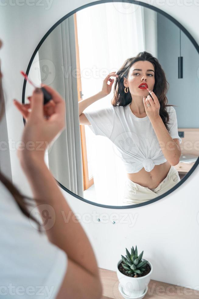 Young woman applying lipstick looking at mirror photo