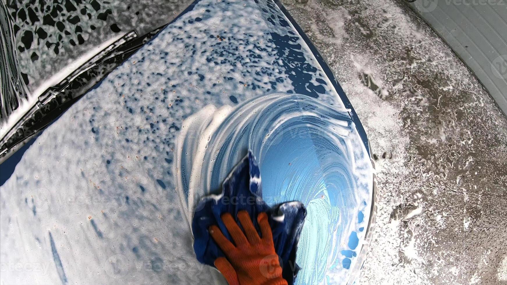 Young man washing his car after shampooing wiping with a cloth photo