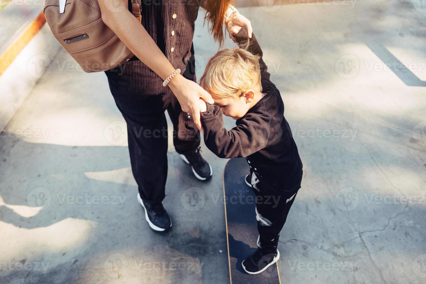 Young mother teaches her little boy to ride a skateboard photo