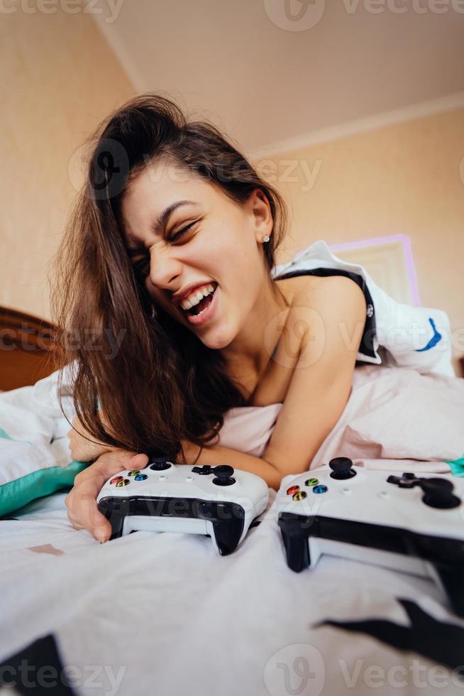 chica divertida acostada en la cama y jugando videojuegos, sosteniendo el controlador foto