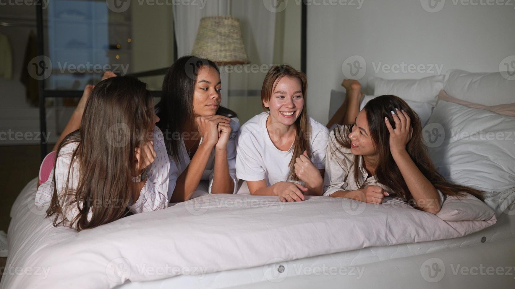 Positive young girls women friends indoors on bed at the hen party at home. photo