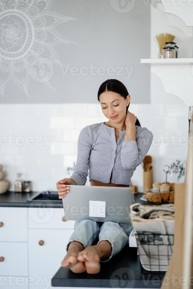 imagen de una linda morena sentada en la cocina y usando una laptop foto