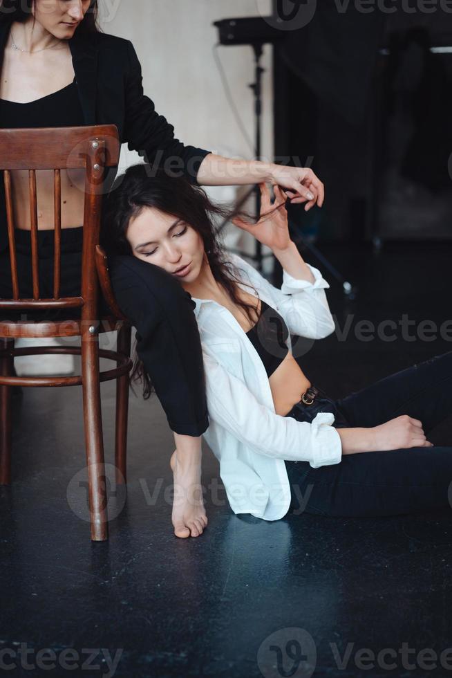 two girls are posing for the camera, one sitting on a chair, other on the floor photo