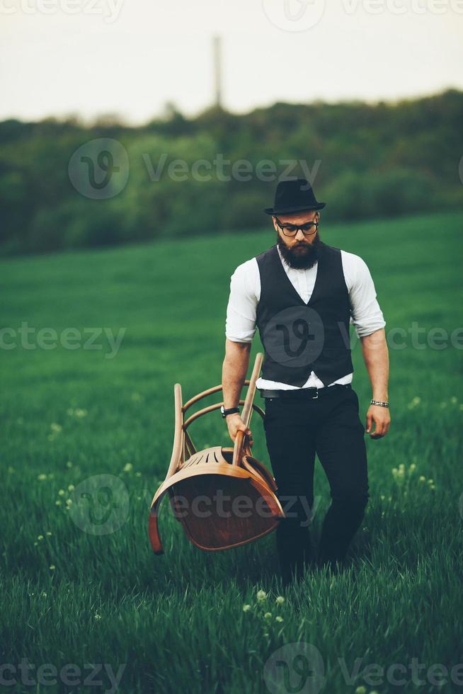 hombre barbudo lleva una silla en el campo foto