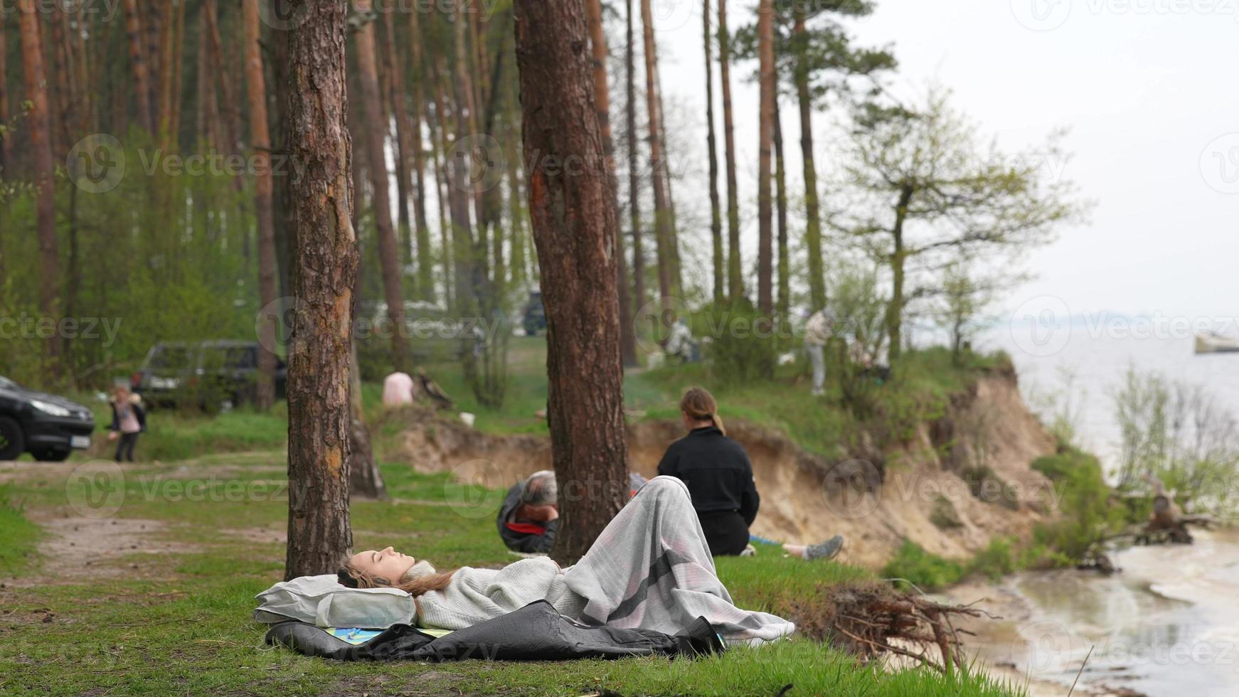 A young woman lies on the shore of a small lake by the forest. photo