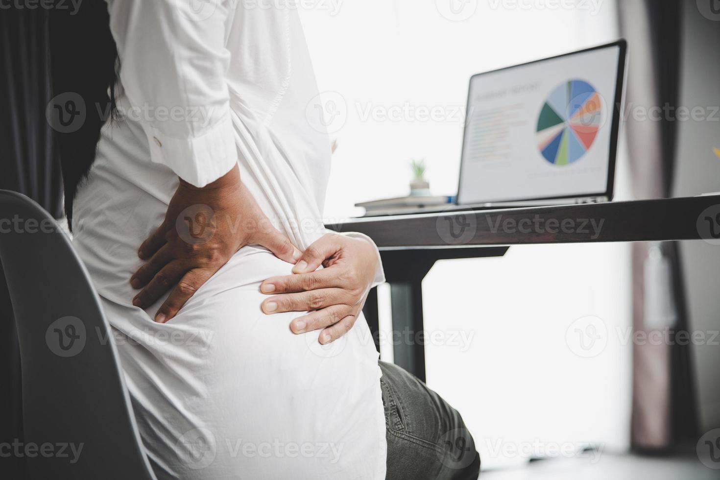 Young asian woman is sitting at work and has tension pain in her neck. Concept office syndrome backache pain from occupational disease, Female having muscle pain from using laptop computer, back pain. photo