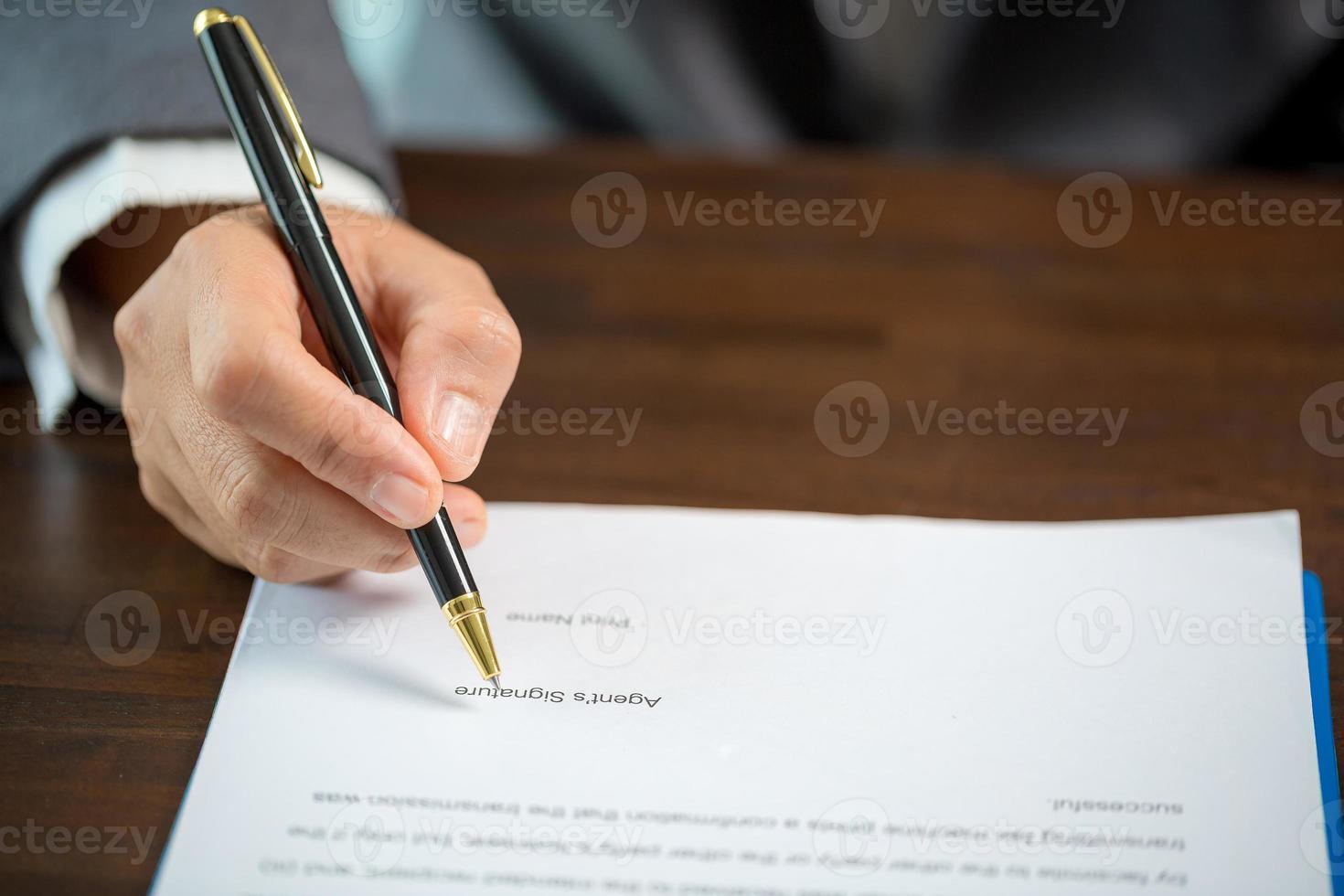 Workplace closeup person professional businesswoman sitting at desk hold pen signing or signature contract paper. Employee woman writing agreement document on paperwork form corporate at work office photo
