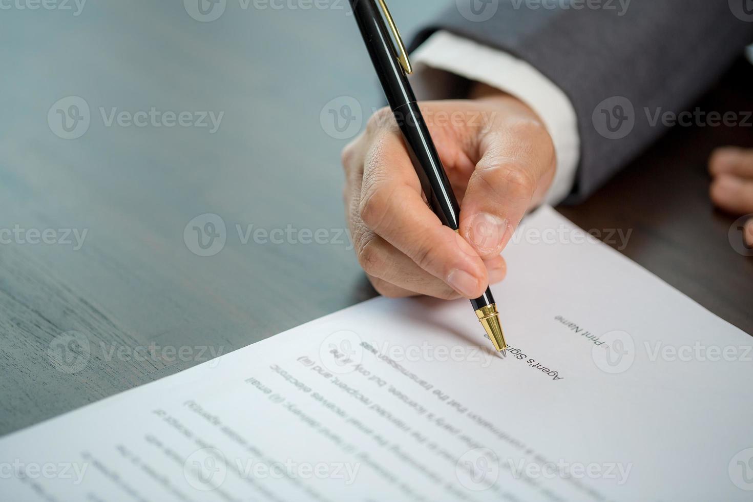 Workplace closeup person professional businesswoman sitting at desk hold pen signing or signature contract paper. Employee woman writing agreement document on paperwork form corporate at work office photo