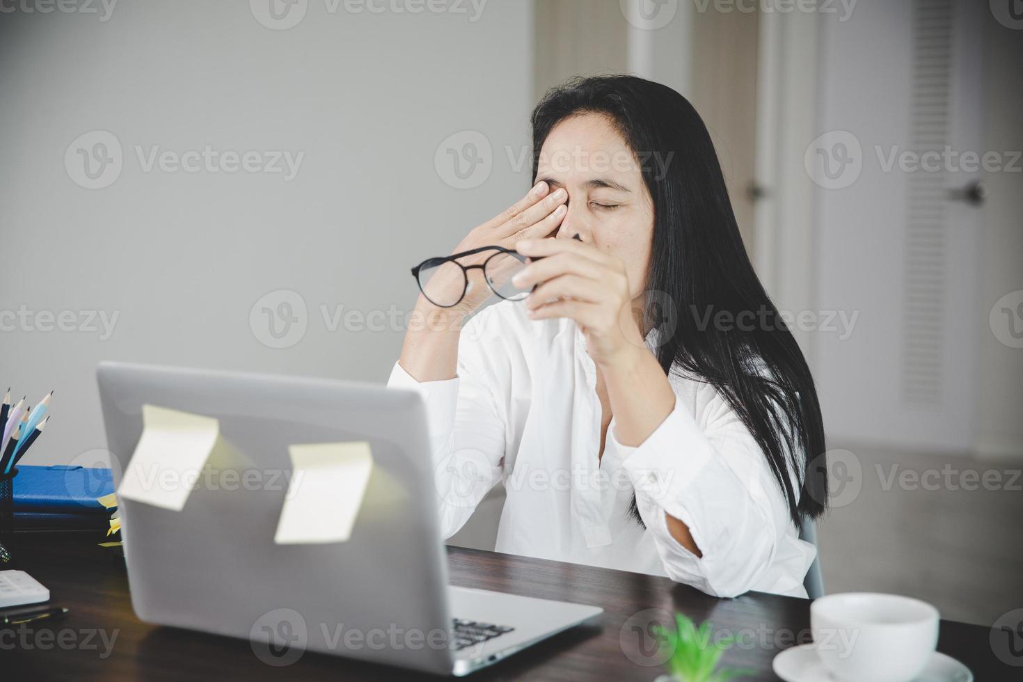 Young business woman person sleepy and has frustration eye problems with cephalalgia disease from using laptop computer on her office desk. Stressed female employee tired and exhausted from overwork. photo