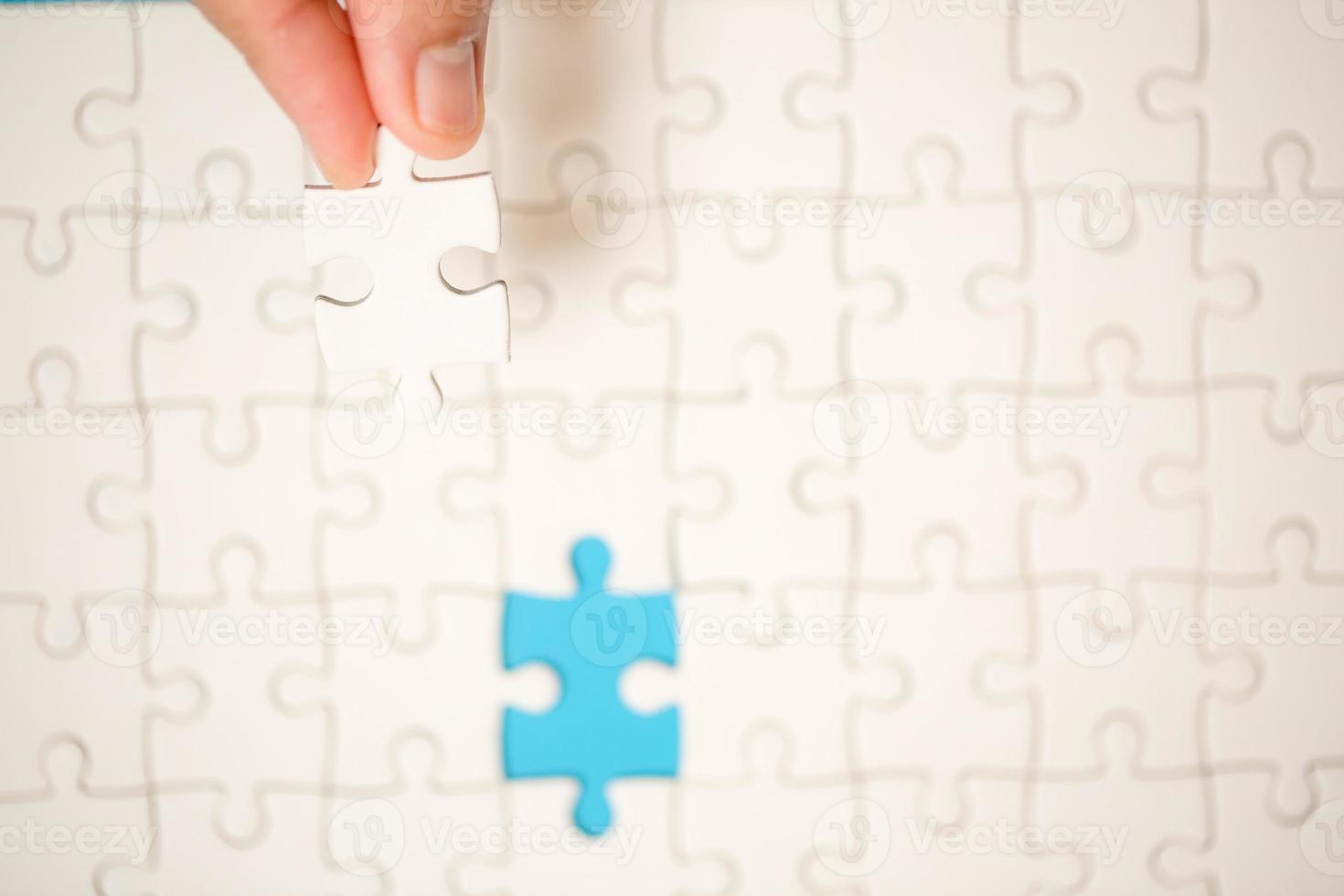 Close up hand holding and playing jigsaw game incomplete. White part of jigsaw puzzle pieces on blue background. concepts of problem solving, business, teamwork. photo