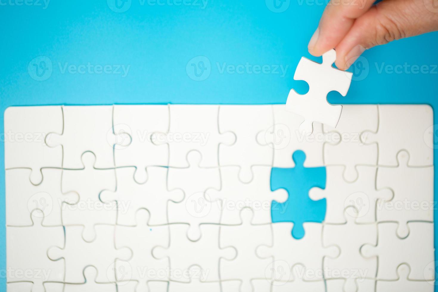 Close up hand holding and playing jigsaw game incomplete. White part of jigsaw puzzle pieces on blue background. concepts of problem solving, business, teamwork. photo