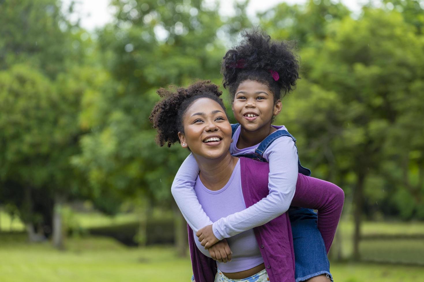 African American mother is playing piggyback riding with her young daughter while having a summer picnic in the public park for wellbeing and happiness concept photo