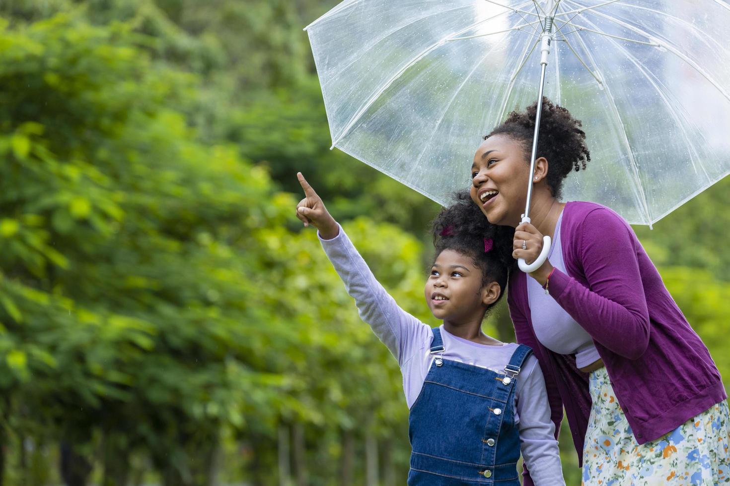 African American mother is enjoy walking with her young daughter with umbrella in the public park for wellbeing and happiness concept photo