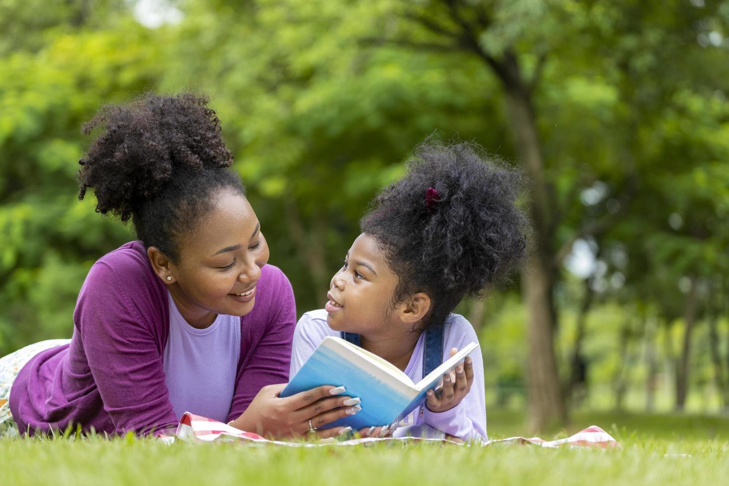 African American mother is teaching her young daughter to read while lying down after having a summer picnic in the public park for education and happiness concept photo