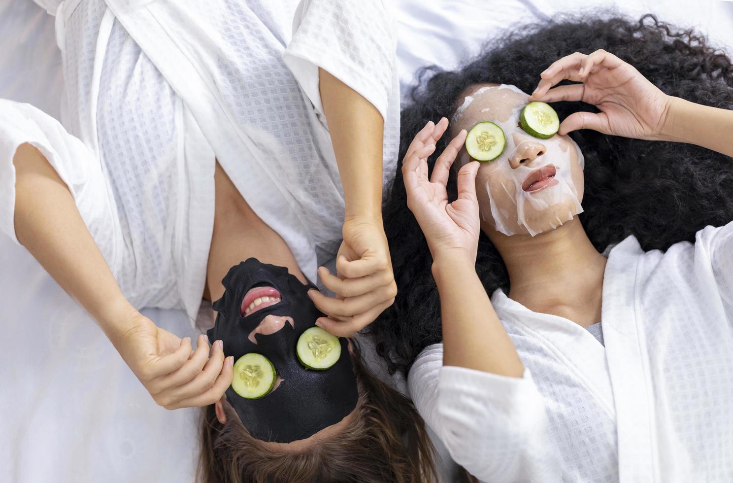 Couple of girlfriend in bathrobe doing skincare routine using facial mask and cucumber slice on spa holiday for beauty skin and treatment concept photo