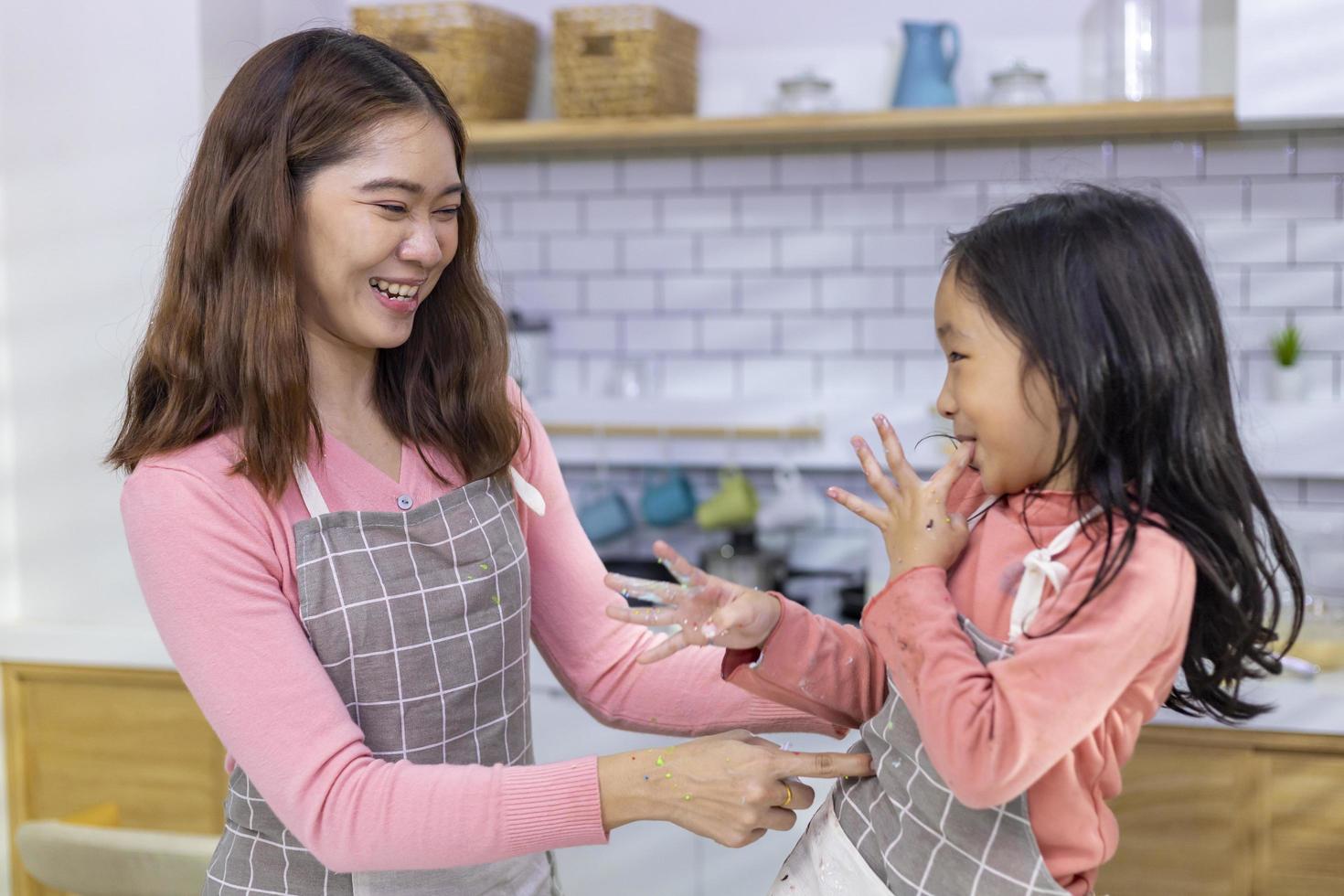 Happy Asian mother is tickling her daughter for having fun time after cooking in the kitchen for love and family concept photo