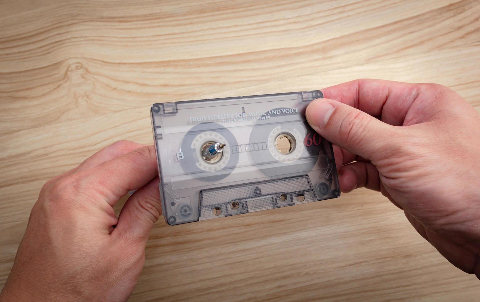 A white man's hand is rewinding cassette tapes on a wooden background. photo