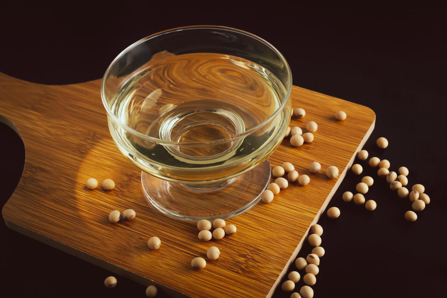 soybean and bowl with oil on a wooden cutting board on black background, front view,selective focus. photo