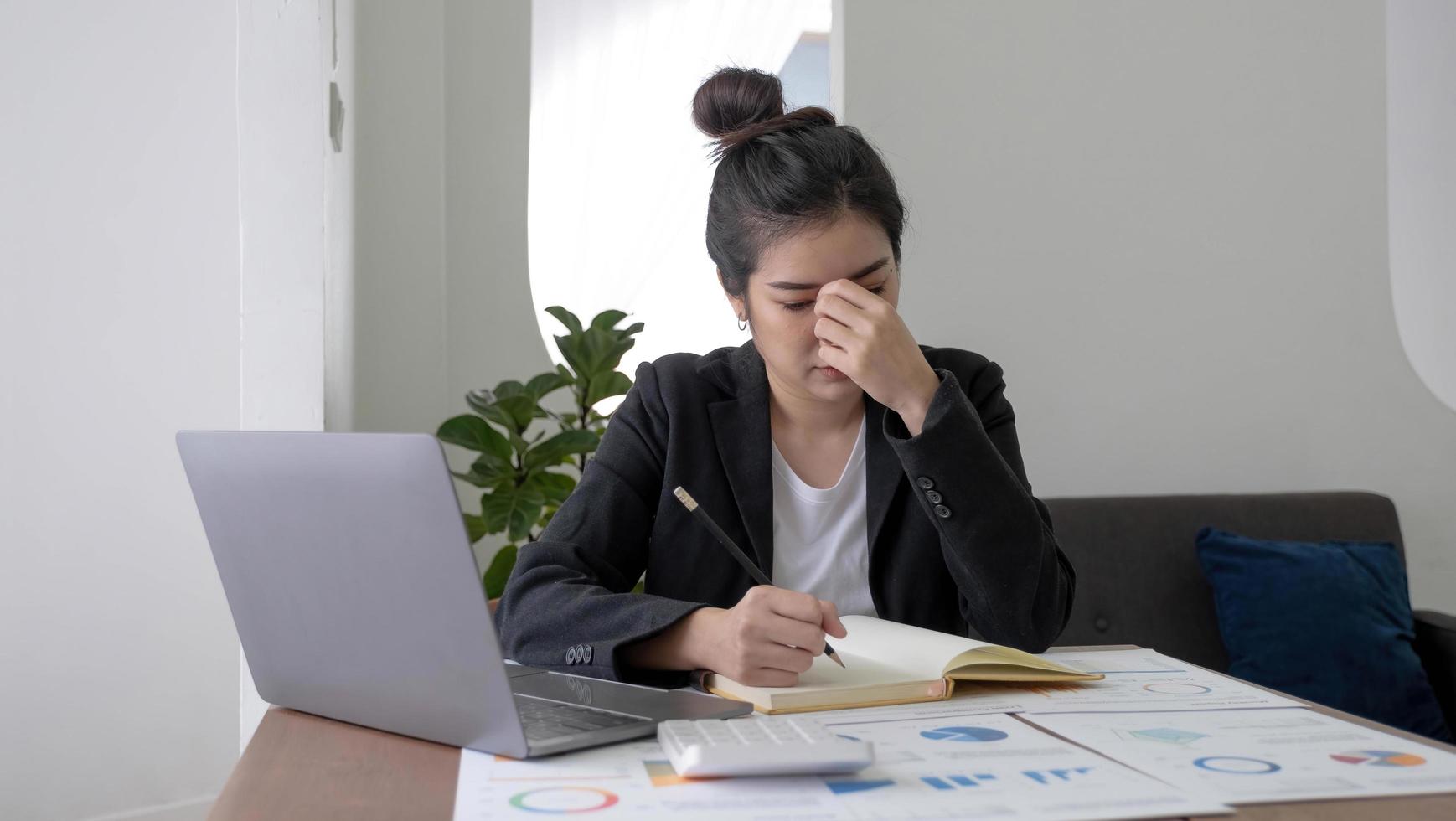 mujer asiática joven que siente tensión en la cabeza con migraña. mujer de negocios cansada y sobrecargada de trabajo mientras trabajaba en una computadora portátil en la oficina. foto