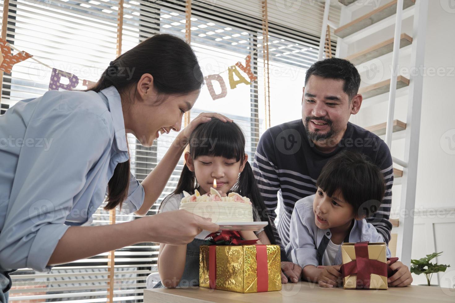 Happy Asian Thai family, young daughter is surprised, birthday cake and lovely gift, girl blows candle, pray and cheerful celebrates party with parents together, special domestic home event lifestyle. photo