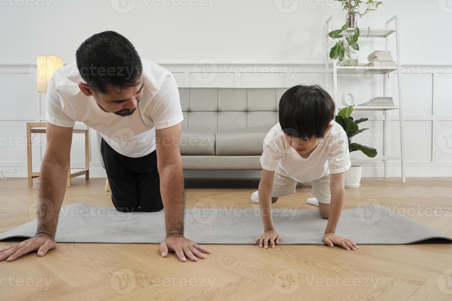 Young Asian Thai father lovely trains her little son to exercise and practices yoga on living room floor together for healthy fitness and wellness, happy domestic home lifestyle on family weekends. photo