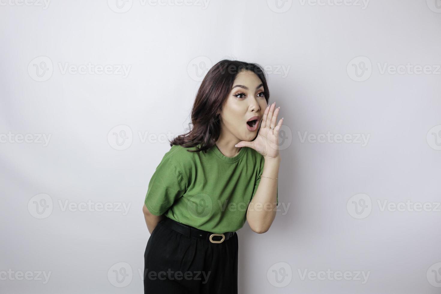 joven mujer hermosa con una camiseta verde gritando y gritando fuerte con una mano en la boca. concepto de comunicación. foto