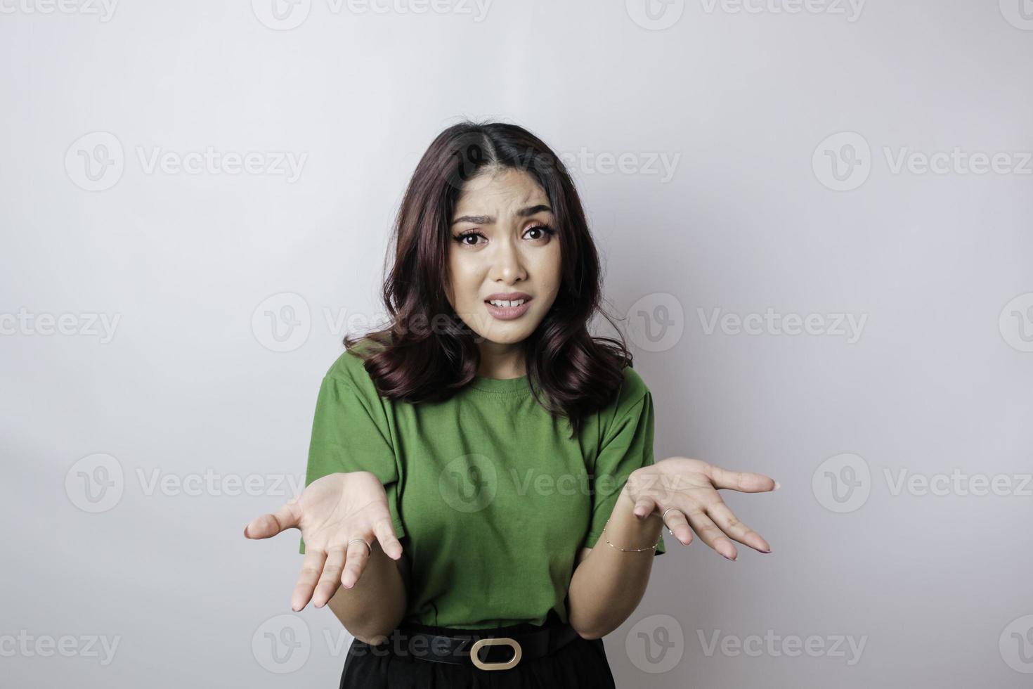 A portrait of an Asian woman wearing a green t-shirt looks so confused, isolated by a white background photo