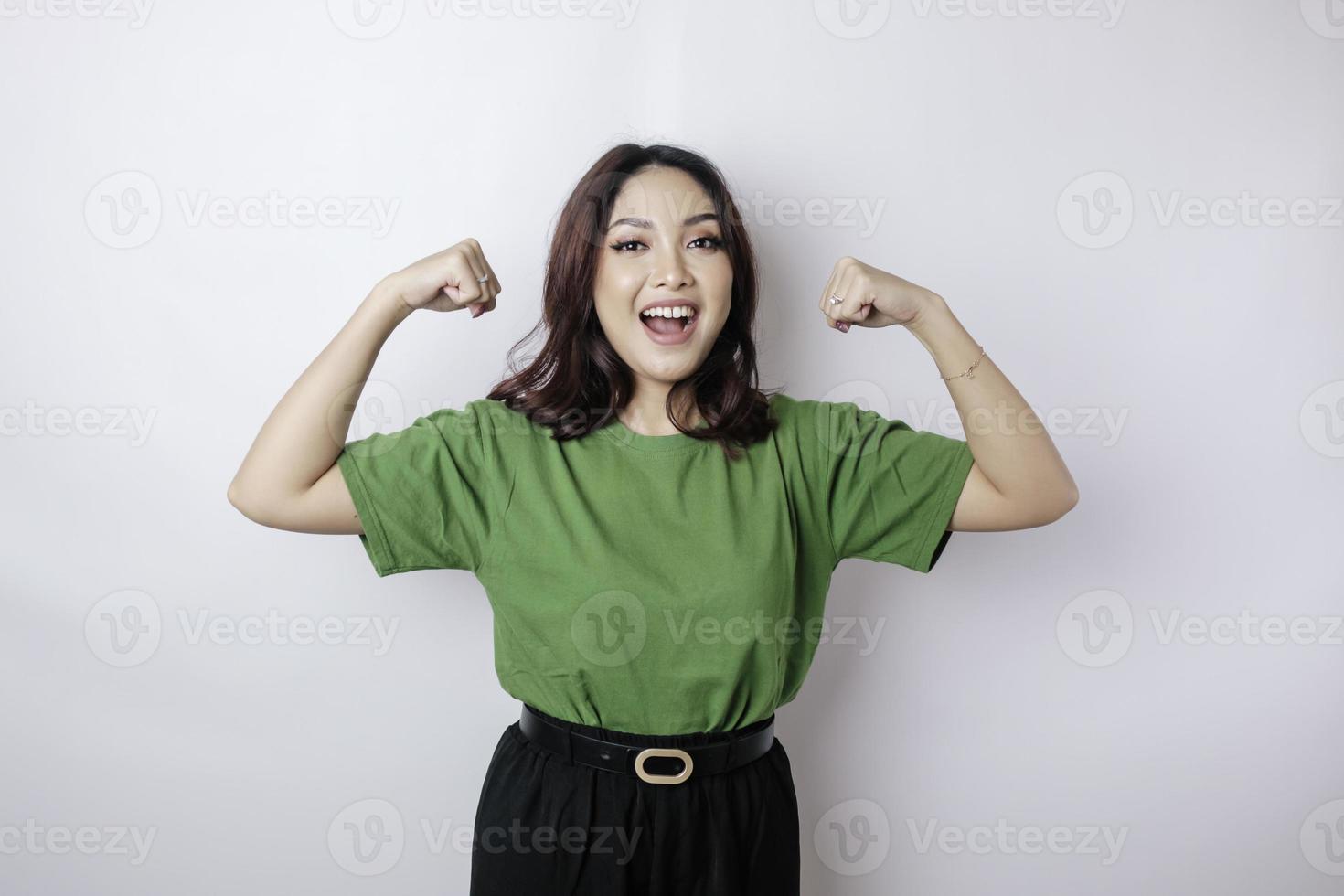 Excited Asian woman wearing a green t-shirt showing strong gesture by lifting her arms and muscles smiling proudly photo