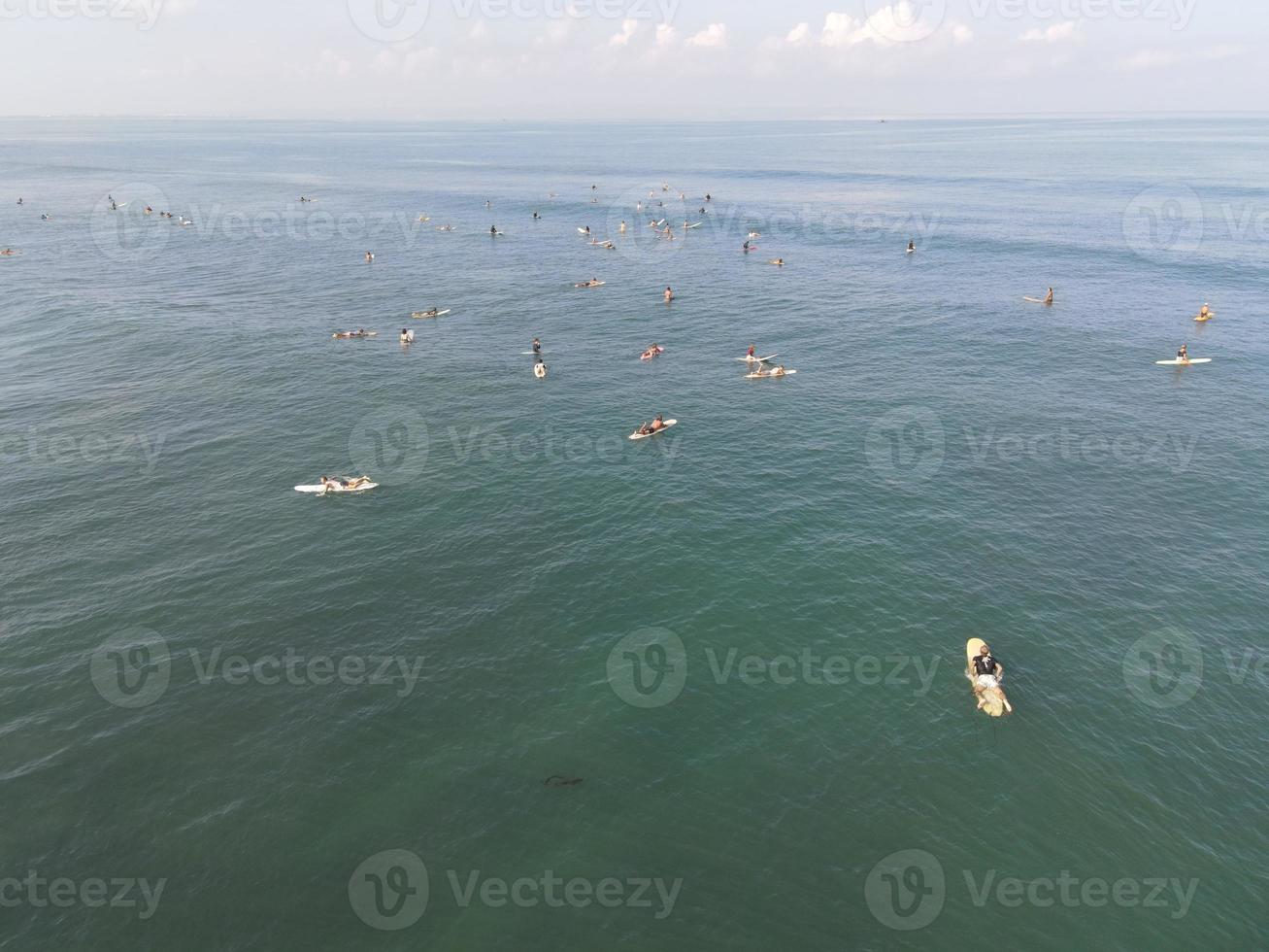 vista aérea de personas surfeando en olas con tablas de surf cuando están de vacaciones en bali, indonesia foto