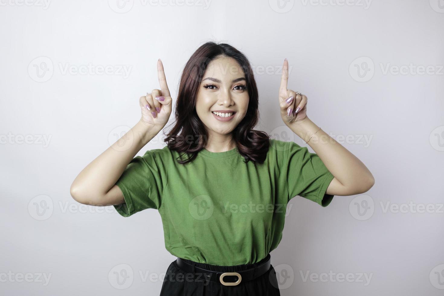 Excited Asian woman wearing green t-shirt pointing at the copy space upside her, isolated by white background photo
