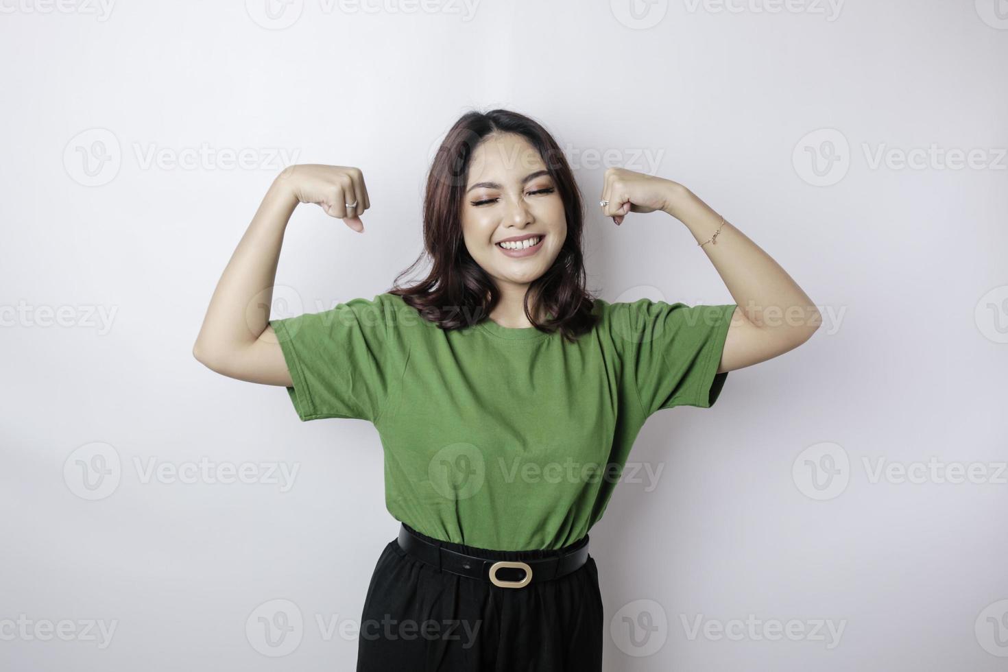 Excited Asian woman wearing a green t-shirt showing strong gesture by lifting her arms and muscles smiling proudly photo