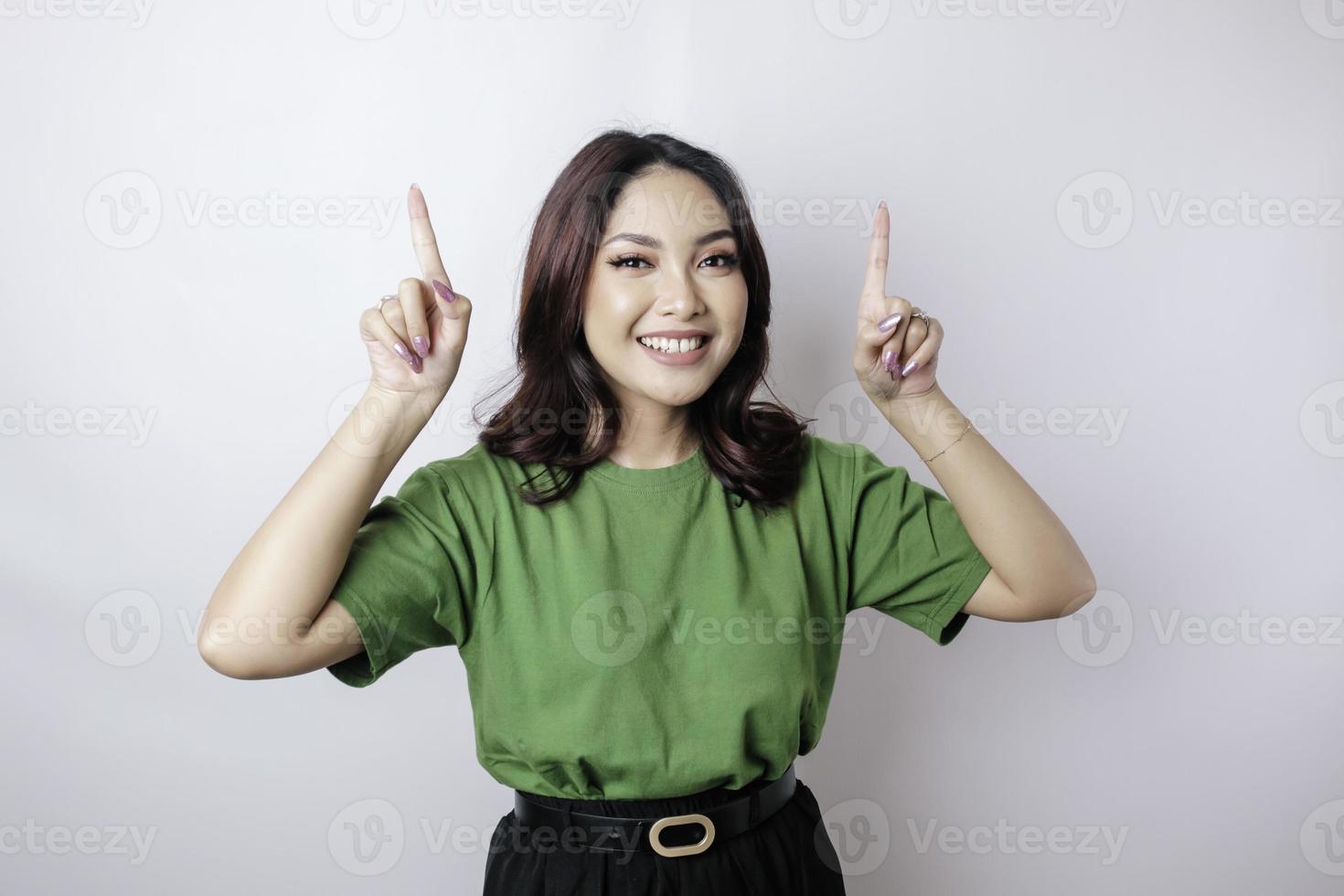 Excited Asian woman wearing green t-shirt pointing at the copy space upside her, isolated by white background photo