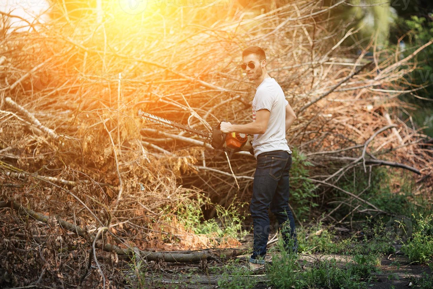 The man in the authentic boots and selvedge jeans with a chainsaw on a the background of branches photo