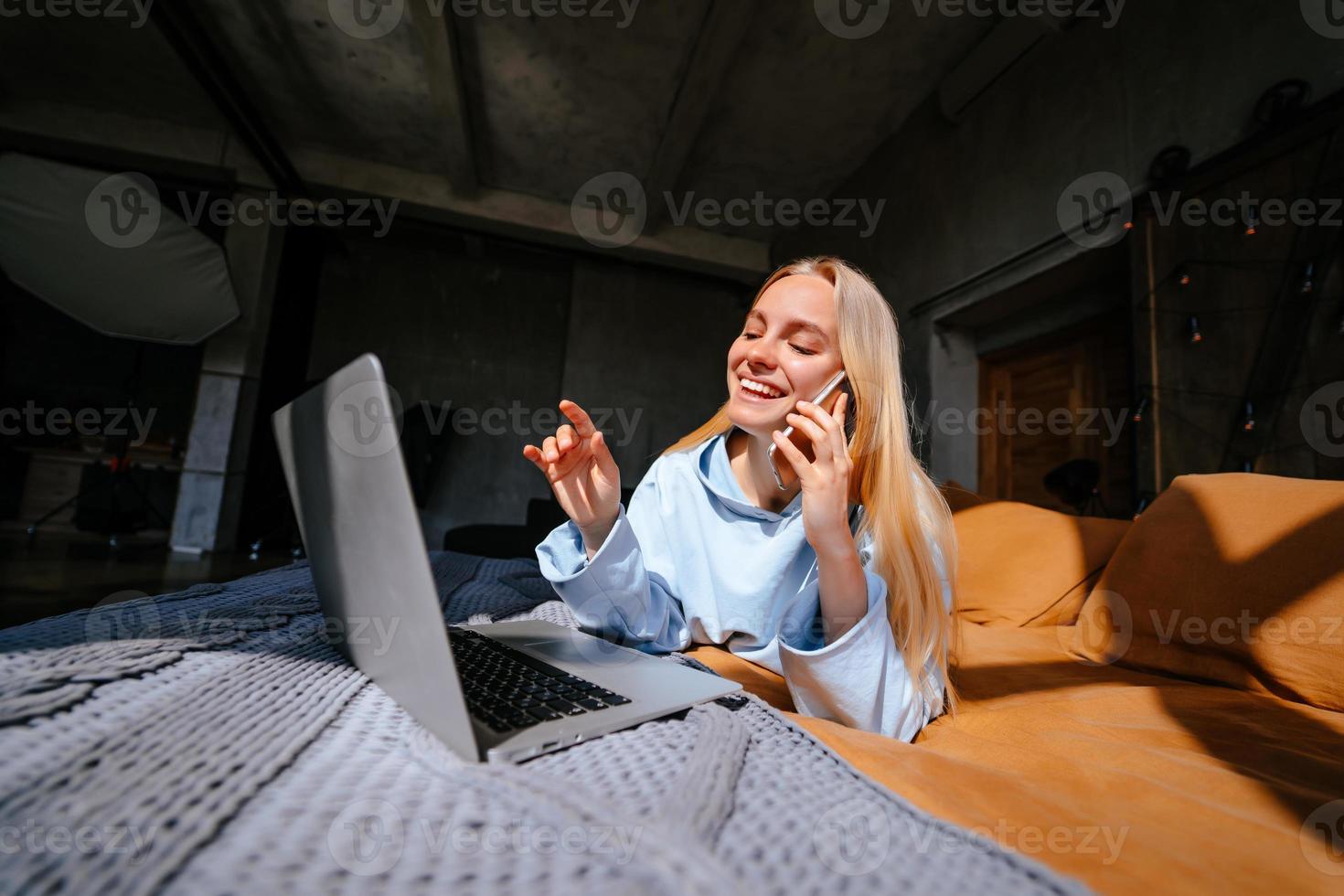 Smiling attractive woman lying on bed talking by smartphone photo