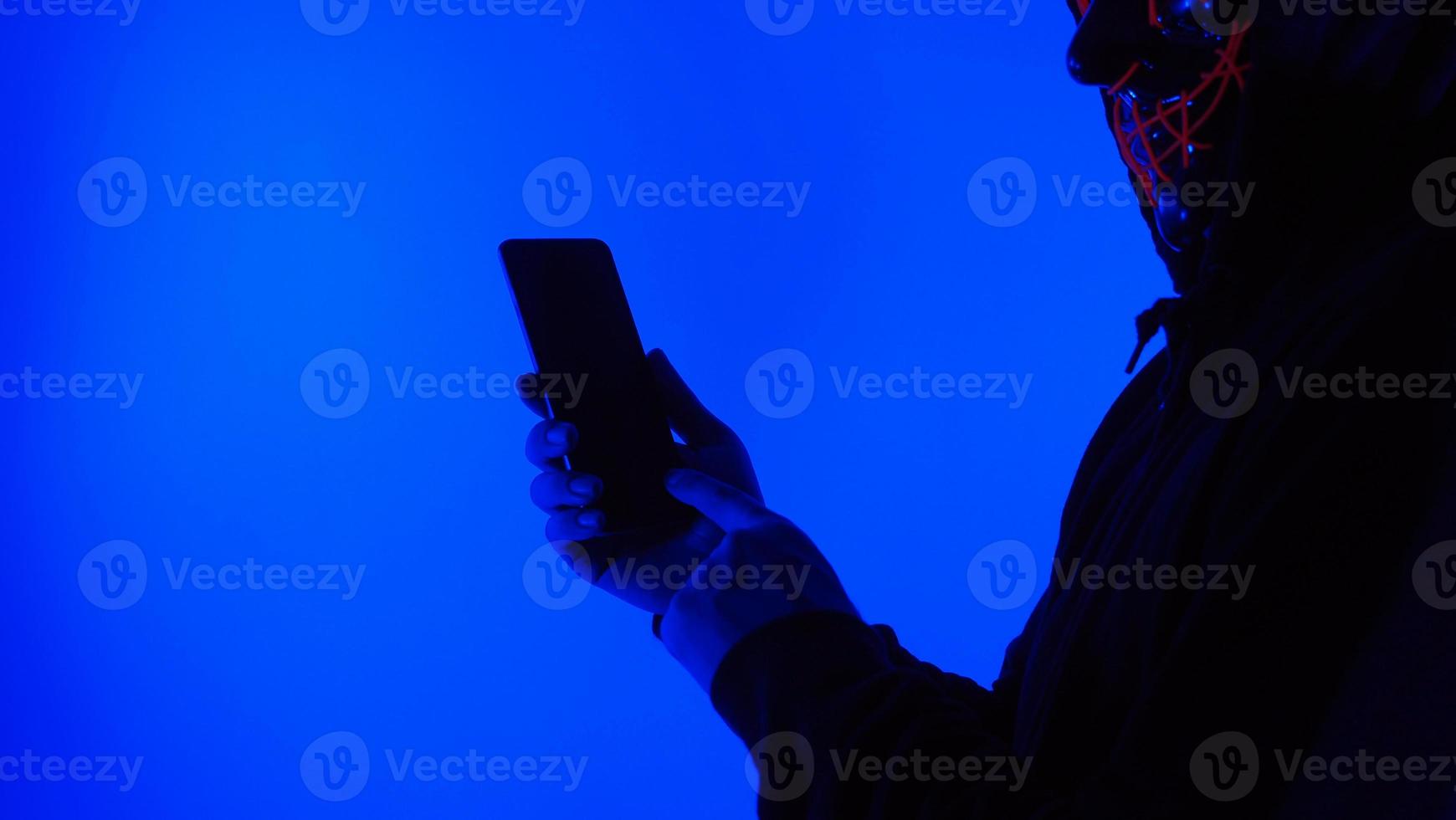 Anonymous hacker and face mask with smartphone in hand. photo