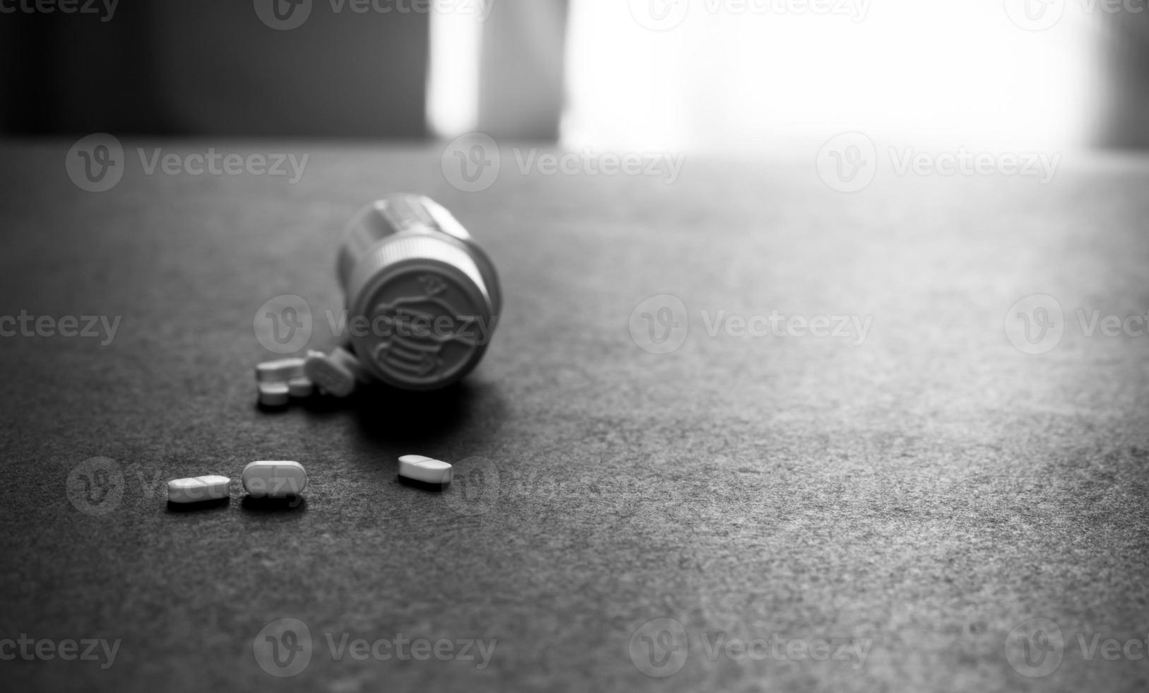 White tablets pills and blur plastic pill bottle on dark floor. Prescription drugs. Pharmaceutical industry. Medical care. Medication for mental illness. Pharmacy. Small white pills. Dose recommended. photo