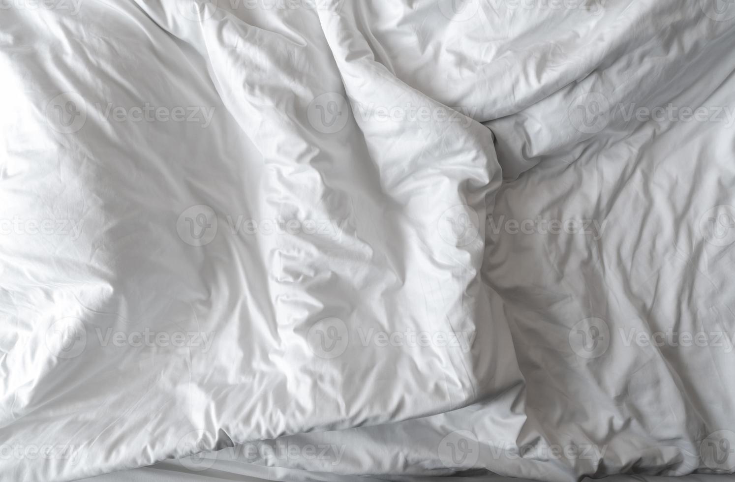 White linen blanket in hotel bedroom. Close-up detail of messy white blanket. Comfortable bed with soft white duvet. Sleep tight with good quality bedding household concept. Wrinkled white blanket. photo