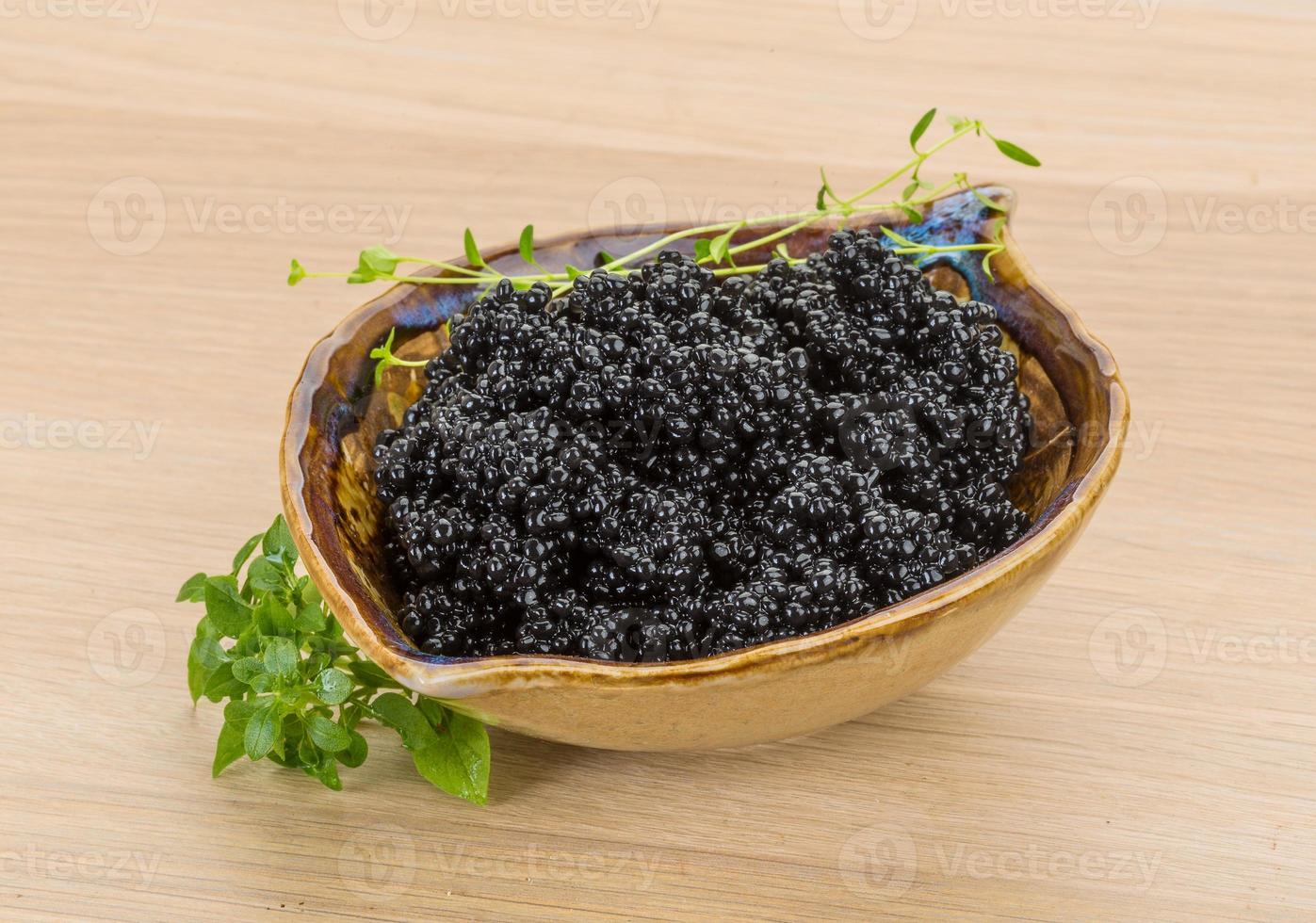 Black caviar in a bowl on wooden background photo
