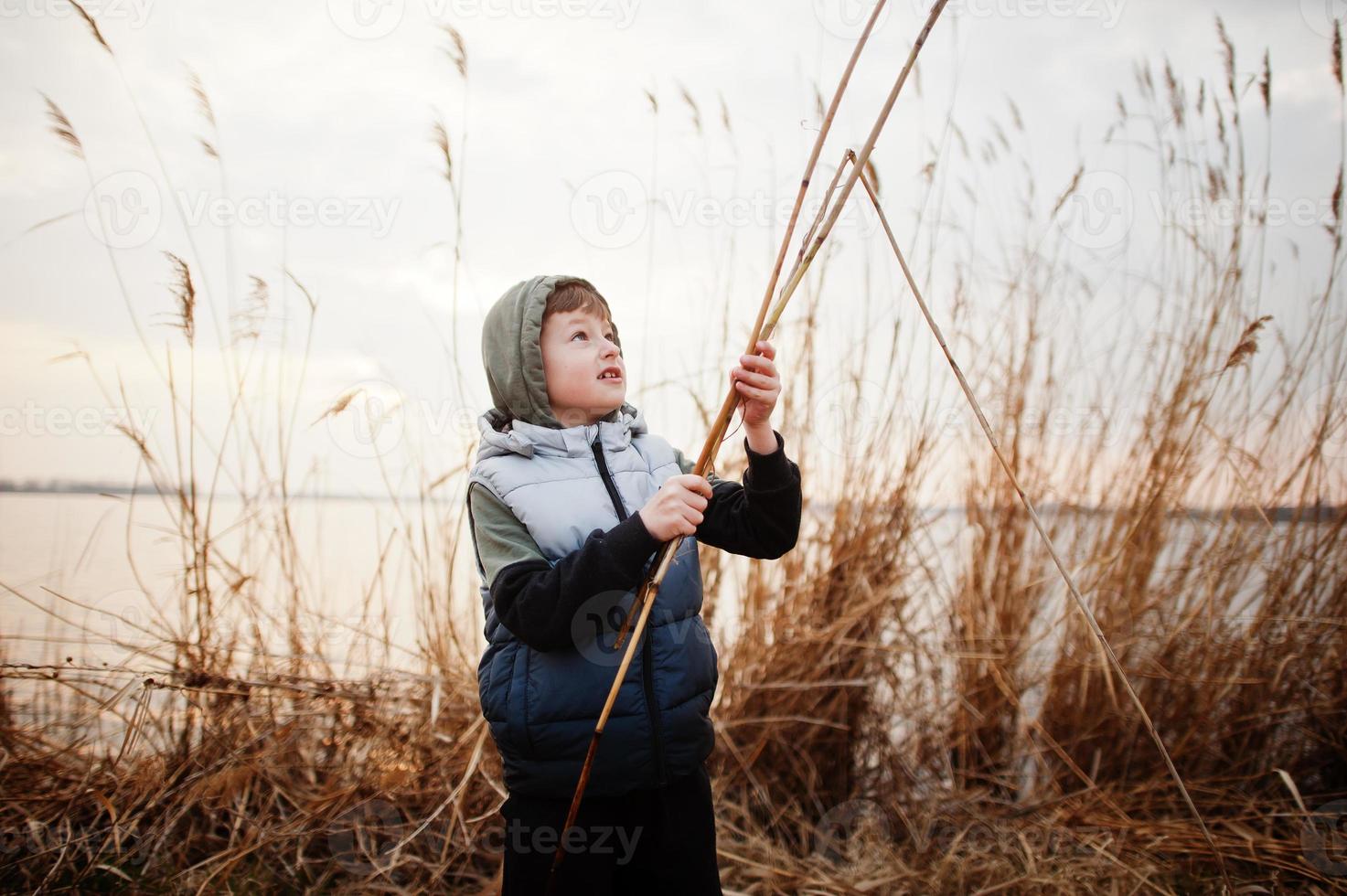 Boy in hoodie by the lake with a reed in his hands. photo