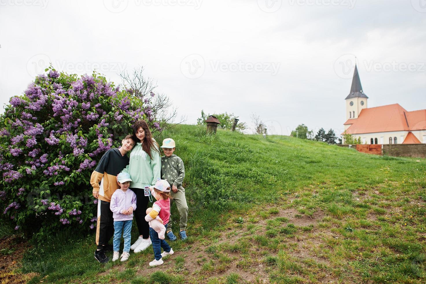 Mother with four kids stand near lilac tree. photo