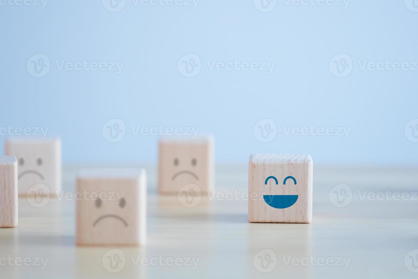 Happy face among unhappy faces on wooden blocks. Positive thinking, Feedback, Satisfaction, Customer service review, Mental health assessment, World mental health day concept. photo