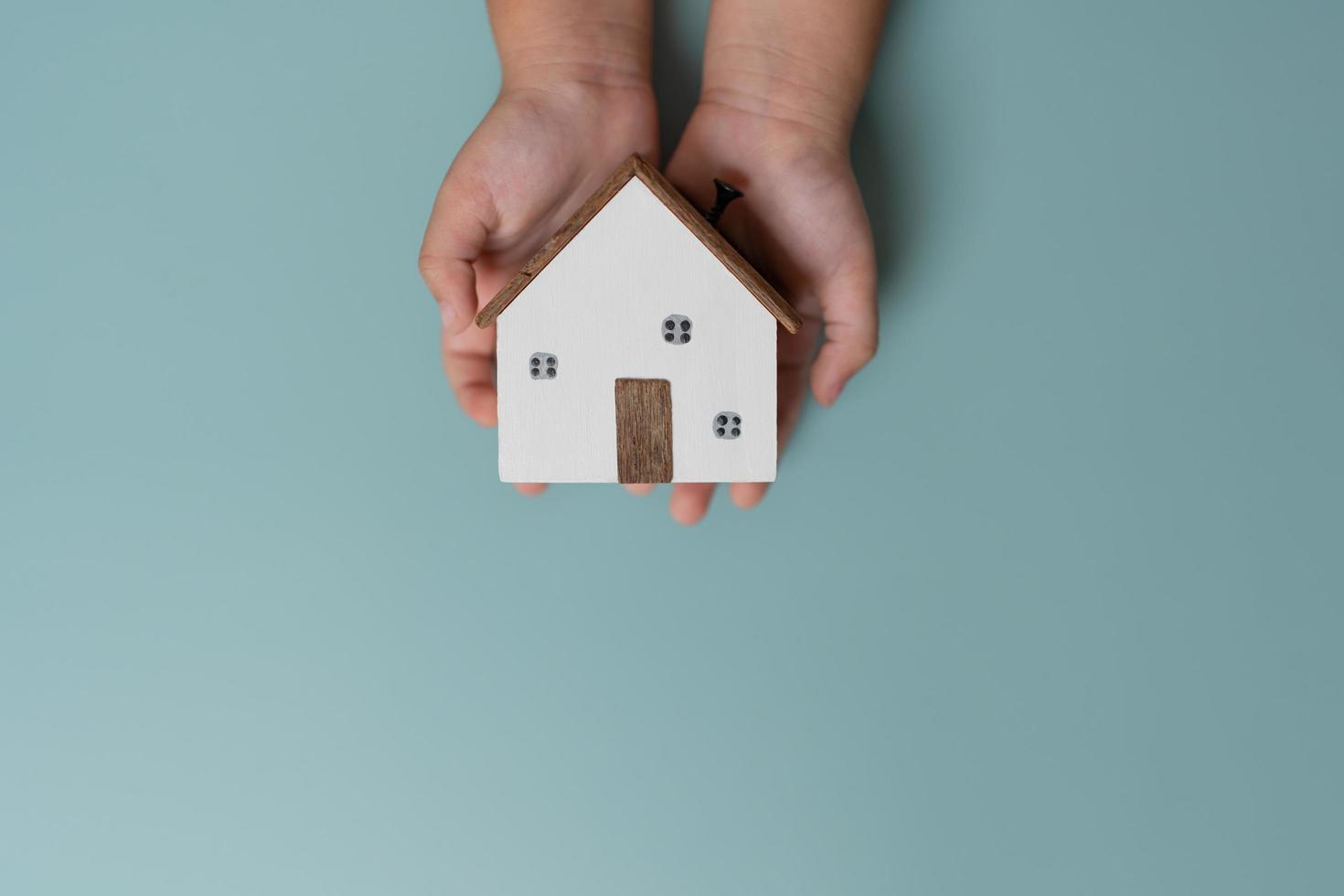 manos de niños sosteniendo una pequeña casa de madera, concepto de vida. foto