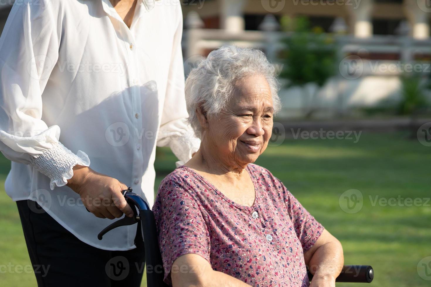 cuidador ayuda y cuida a una anciana asiática o anciana paciente sentada en silla de ruedas en el parque, concepto médico fuerte y saludable. foto