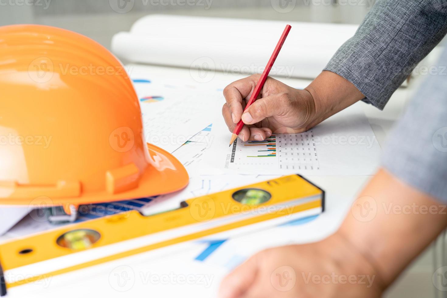 Asian engineer with architectural house plan project blueprint, graph and yellow helmet and engineering construction tools. photo