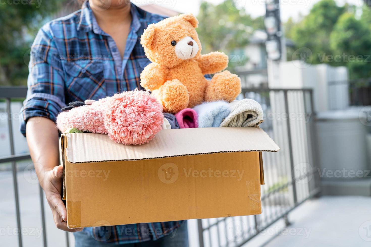 Holding clothing donation box with used clothes and doll at home to support help for poor people in the world. photo