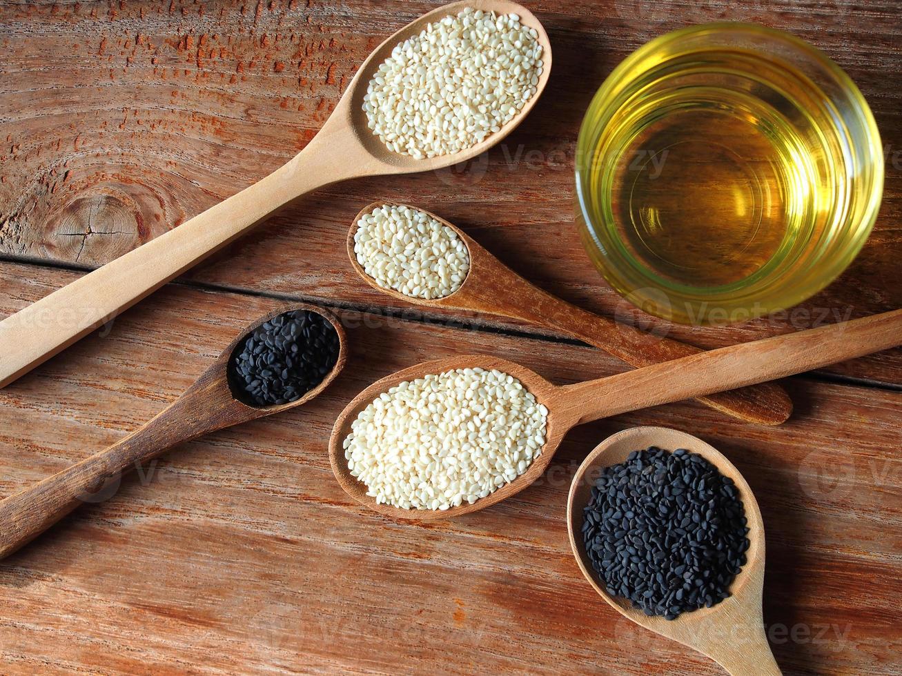 White and black sesame seeds in wooden spoon and a glass of oil photo