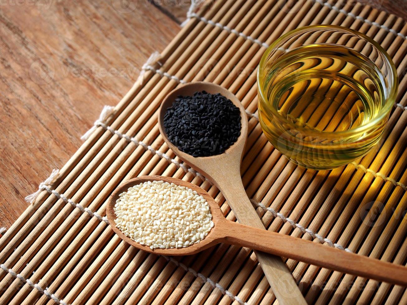 White and black sesame seeds in wooden spoon and a glass of oil photo