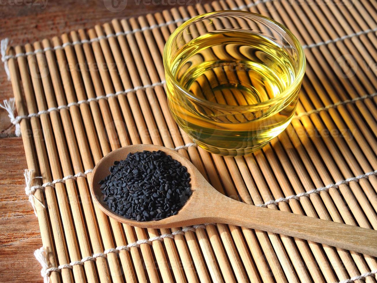 Black sesame seeds in wooden spoon and a glass of oil. photo