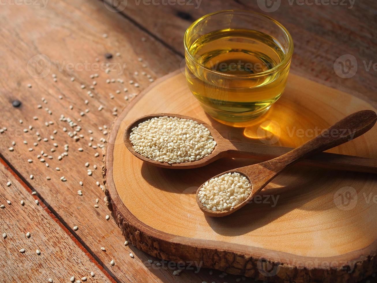 White sesame seeds in wooden spoon and a glass of sesame oil for healthy food concept. photo